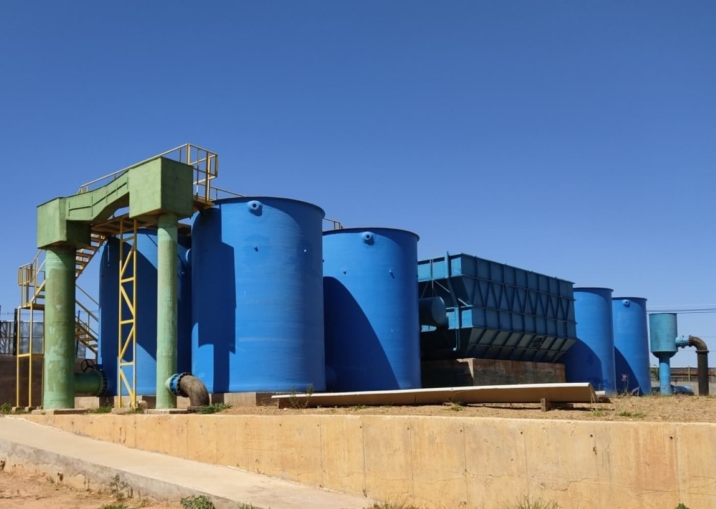 Tanques azuis cilíndricos de uma estação de tratamento de água sob céu claro.