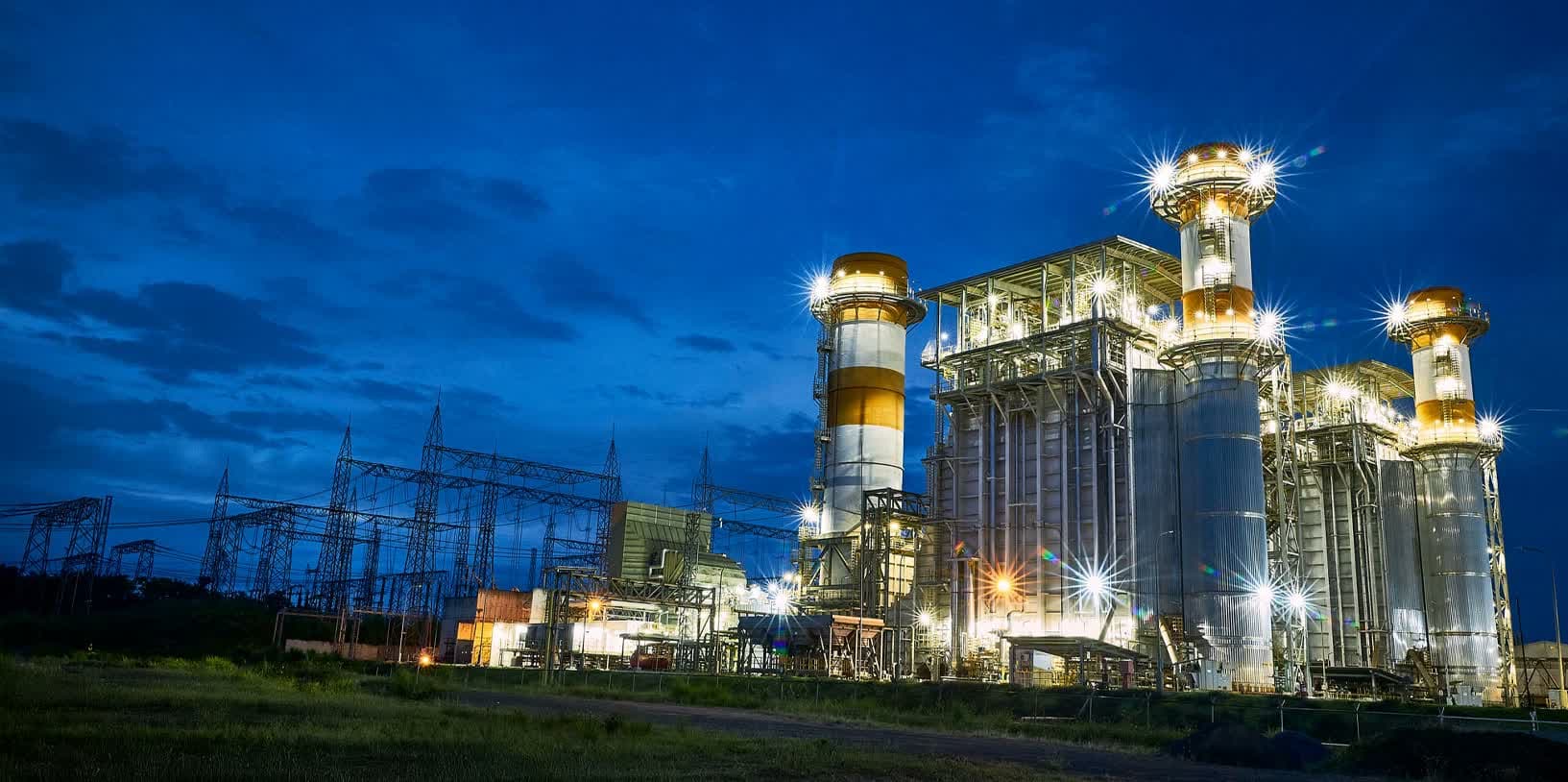 Usina termoelétrica da Eneva iluminada ao anoitecer, destacando as chaminés e a estrutura industrial.