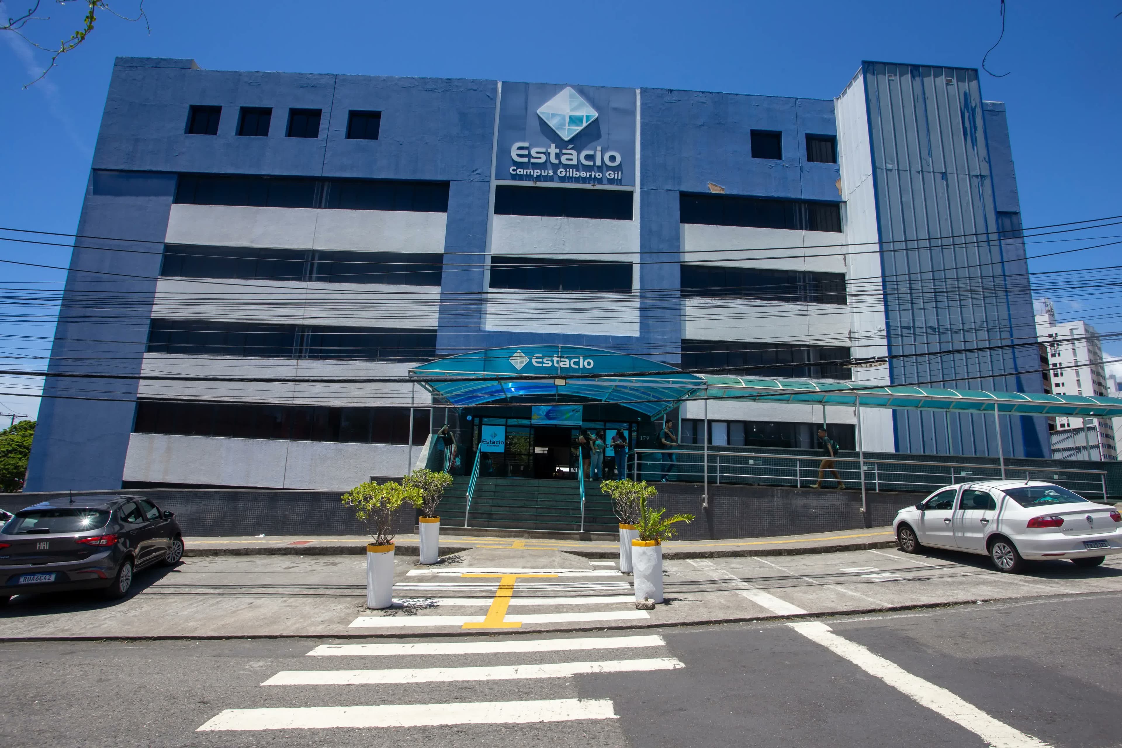 Fachada do prédio de um campus da universidade Estácio, pertencente à Yduqs, sob céu azul.