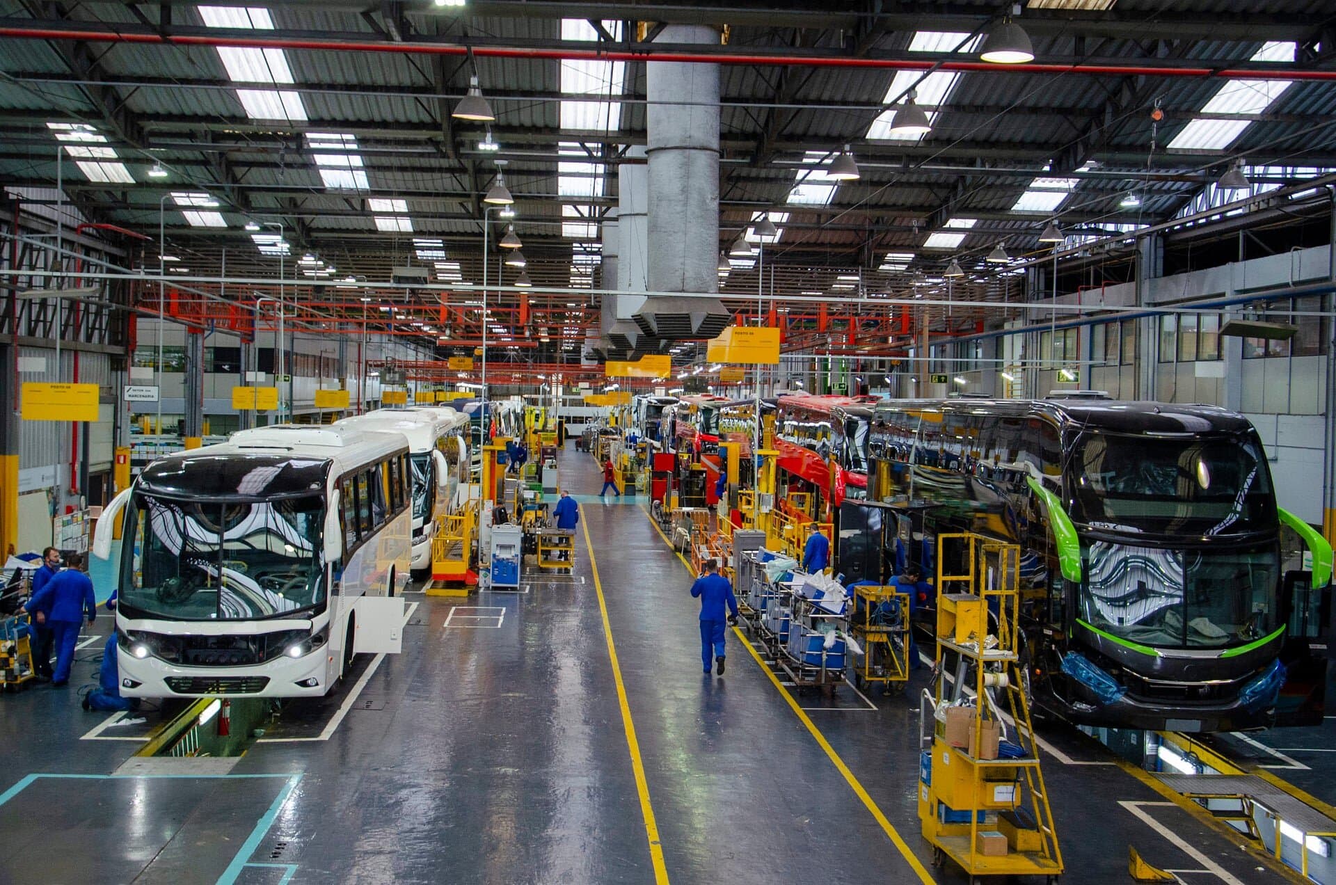 Linha de montagem de ônibus na fábrica da Marcopolo, com veículos em diferentes estágios de produção.