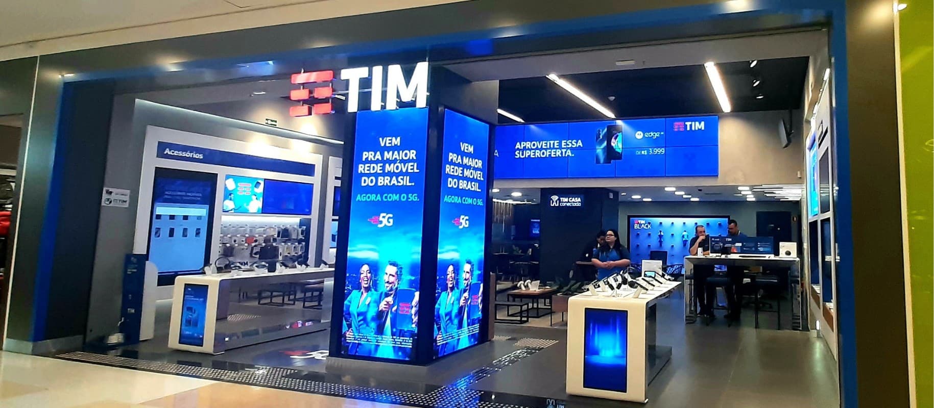 Fachada iluminada de loja da TIM em shopping com painéis digitais destacando a tecnologia 5G.